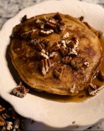 Apple butter sourdough pancakes with butter, maple syrup, and chopped pecans on white plate beside pecans and butter on fork