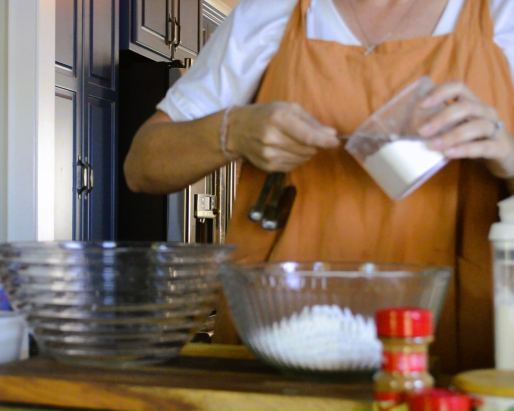 woman putting pancake ingredients into glass mixing bowl with measuring spoon