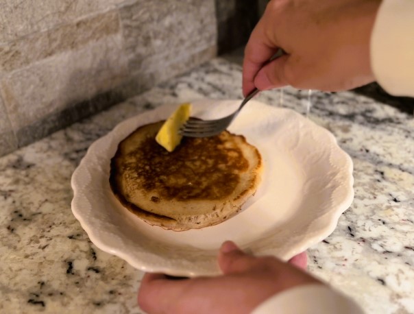 hand using fork to rub butter onto apple butter sourdough pancakes on white plate