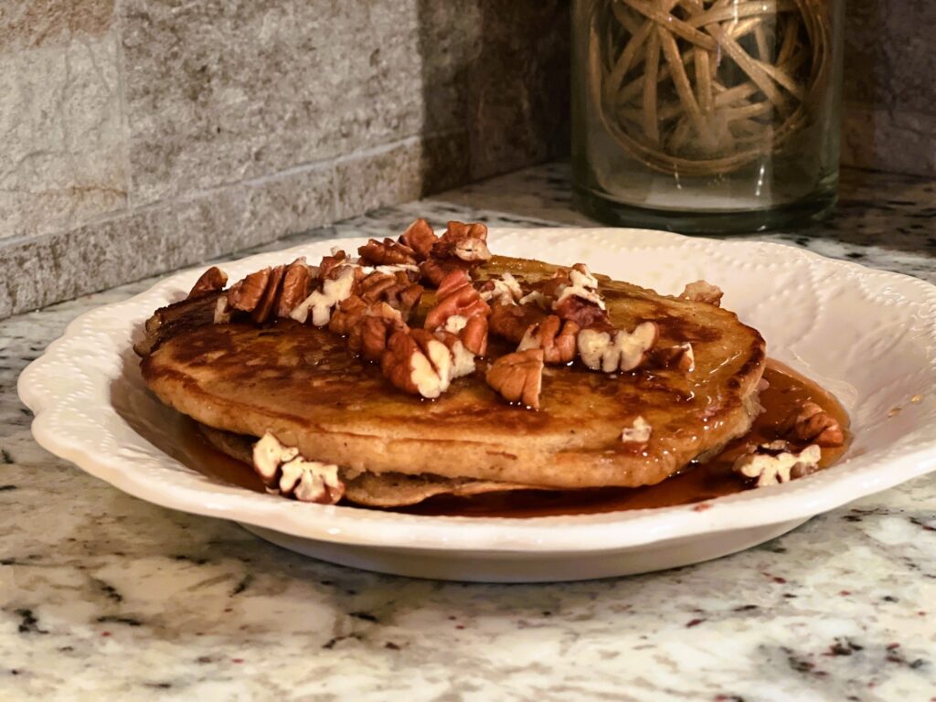 two apple butter sourdough discard pancake with butter, maple syrup, and chopped pecans on a white plate