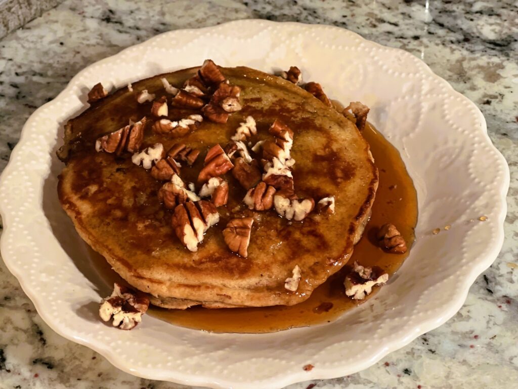 apple butter sourdough pancake with butter, maple syrup, and chopped pecans on a white plate