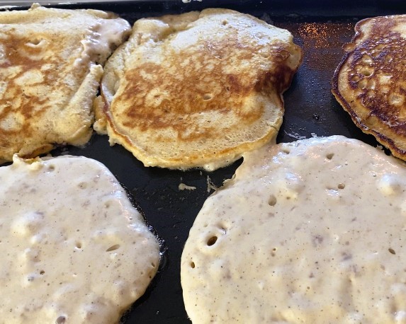 Five apple butter sourdough pancakes cooking on a skillet