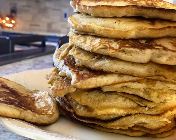 twelve apple butter sourdough pancakes stacked on white plate