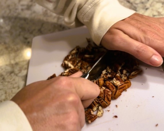 woman chopping up pecans with knife on white cutting board