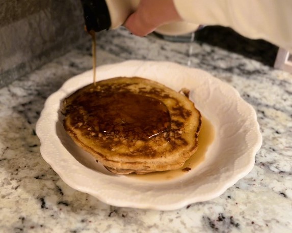 hand pouring maple syrup onto apple butter sourdough pancakes on white plate