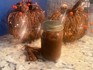 Apple butter in jar beside cinnamon sticks in front of lite up pumpkins