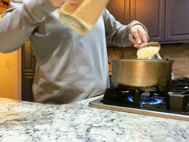 lady pouring couscous into pot over stove
