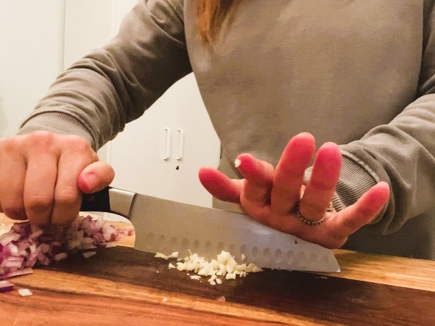 woman dicing garlic with knife on cutting board