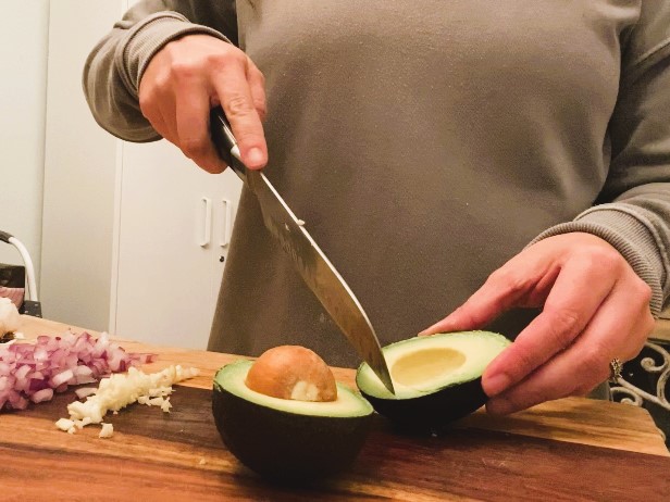 lady cutting an avocado on cutting board with a knife