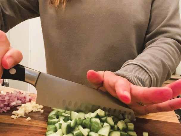 woman dicing cucumbers with knife on cutting board