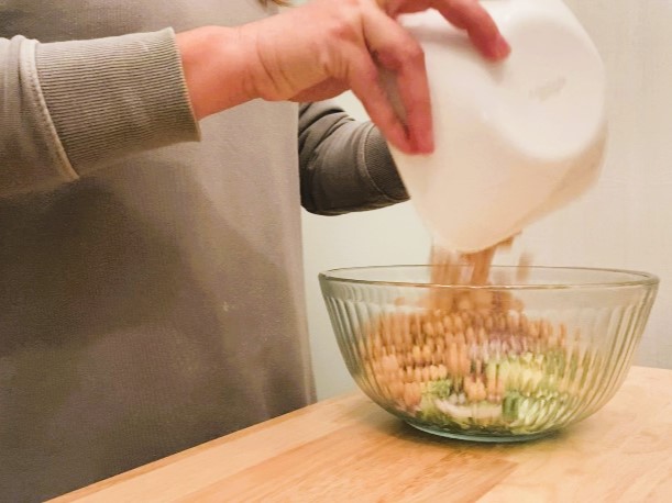 woman pouring chickpeas on top of salad in glass bowl
