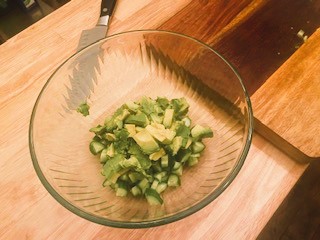 diced cucumbers and avocado in glass bowl on cutting board