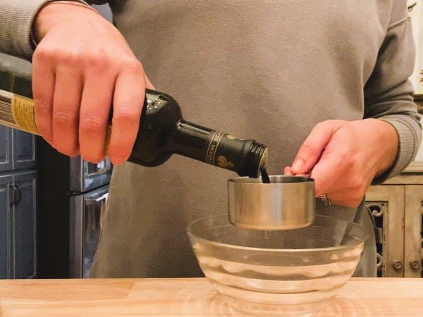 woman pouring balsamic vinegar into measuring cup over glass bowl