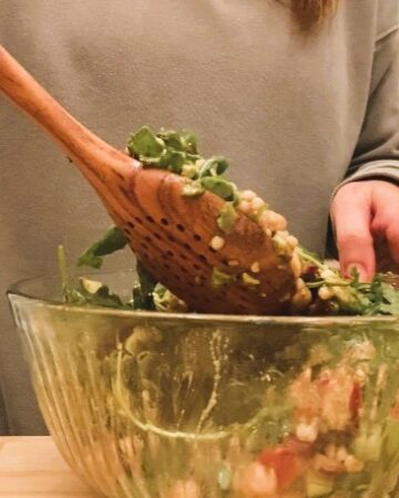 woman stirring Mediterranean couscous salad in glass bowl with wooden spoon