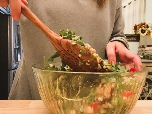 woman stirring Mediterranean couscous salad in glass bowl with wooden spoon