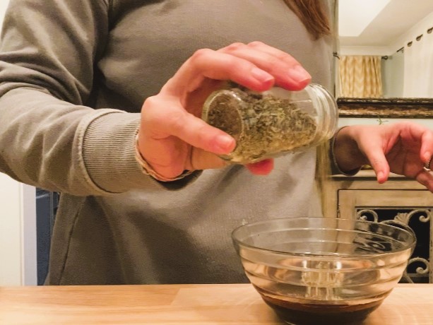 woman sprinkling herbs into glass bowl