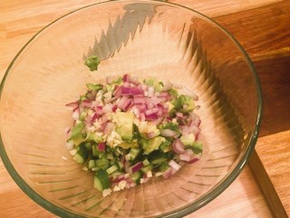 diced cucumber, avocado, onion, and garlic in glass bowl on cutting board