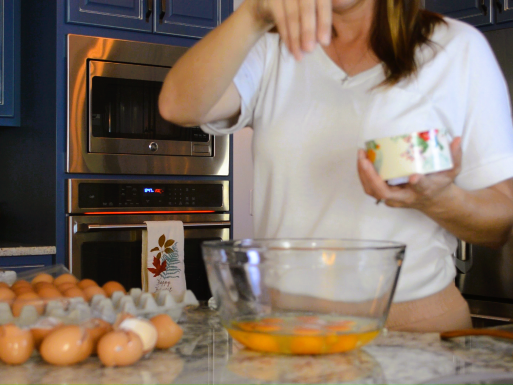 woman sprinkling salt on eggs in glass mixing bowl