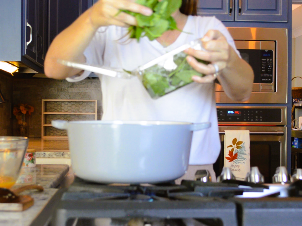 woman dropping spinach into dutch oven on stove top