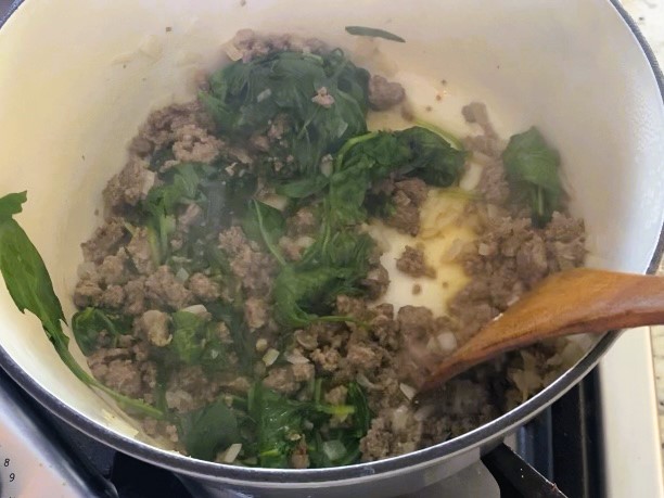 sausage and spinach cooking in dutch oven with wooden spatula