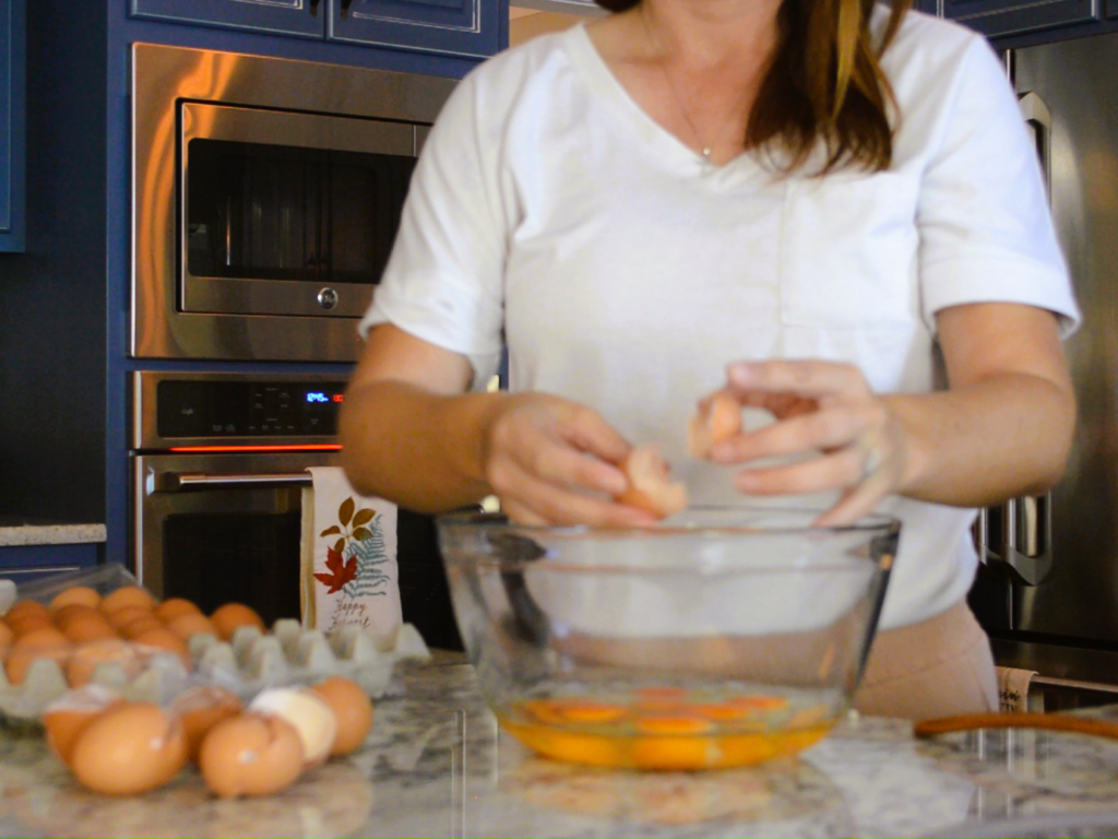 woman cracking eggs into glass mixing bowl